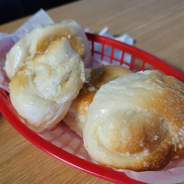 Golden-brown garlic knots in a red basket with white checkered paper, on a wooden table.