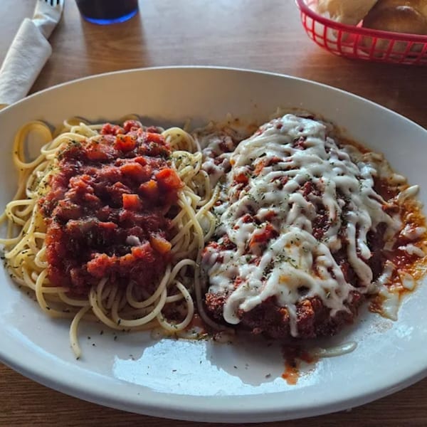 A plate of Mama Mia's chicken parmesan with spaghetti and marinara sauce, and a bread basket.