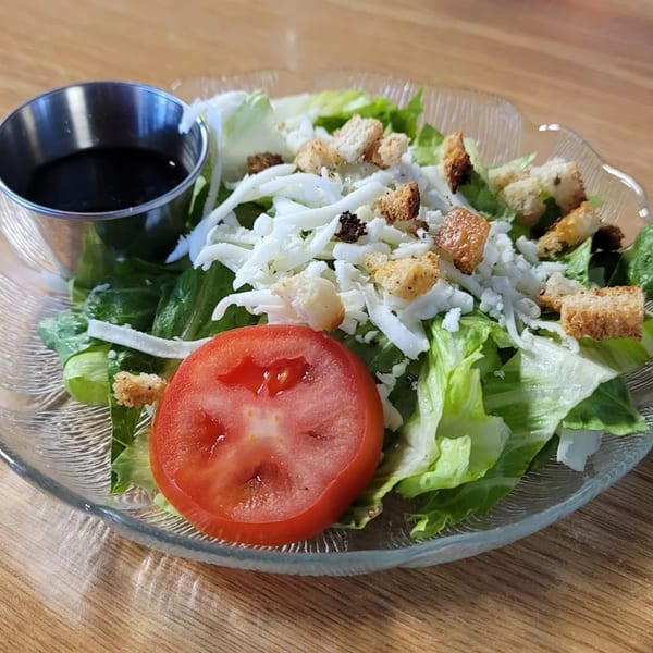 A fresh side salad with lettuce, shredded cheese, croutons, a tomato slice, and balsamic dressing.