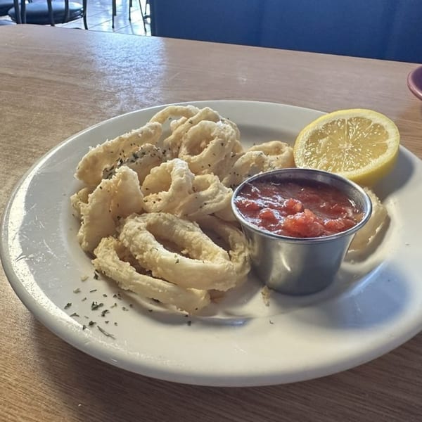Fried calamari with a side of marinara sauce and a lemon wedge on a white plate.